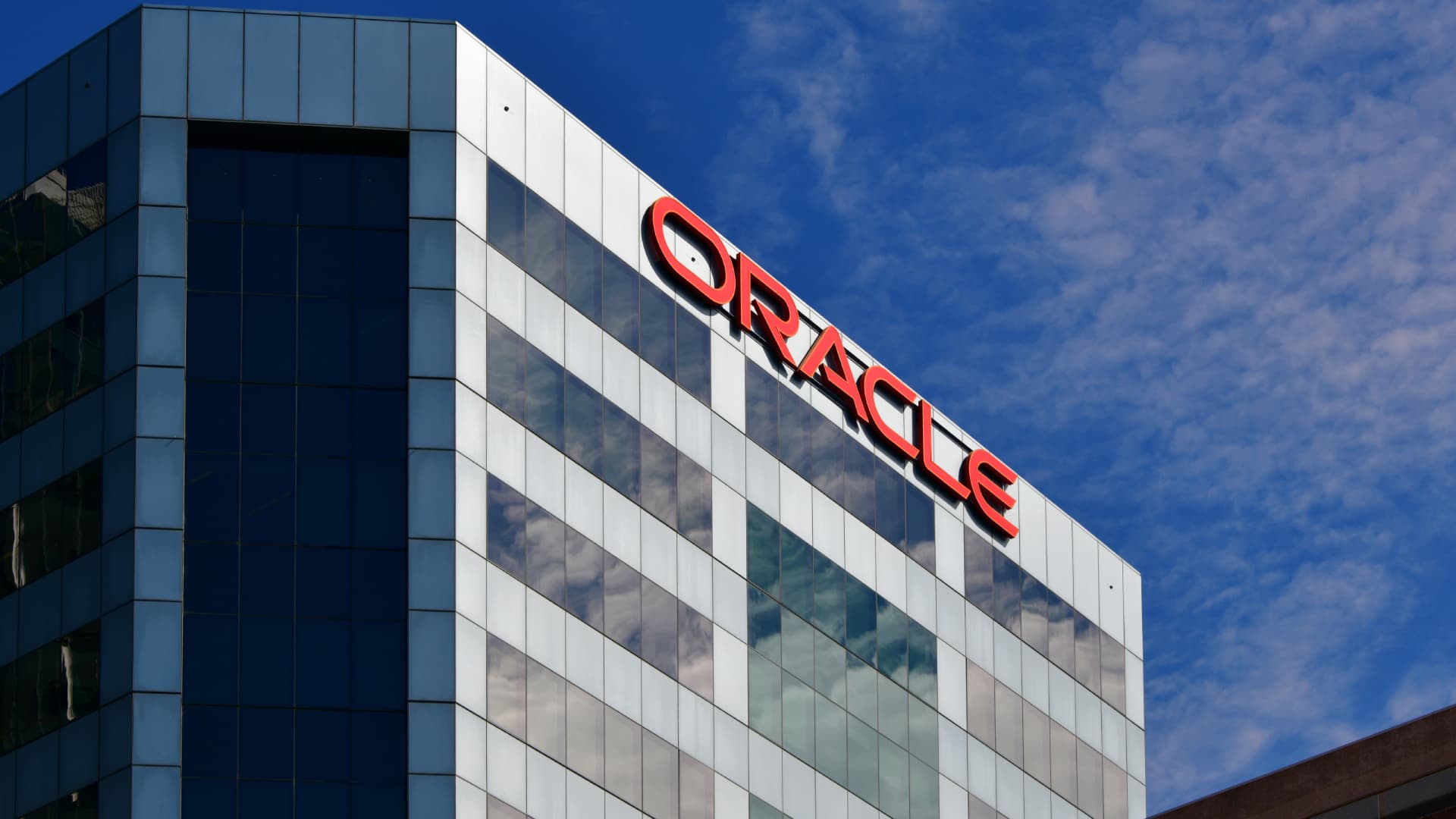 The Oracle logo in red letters near the top of a glass office building against a blue sky.