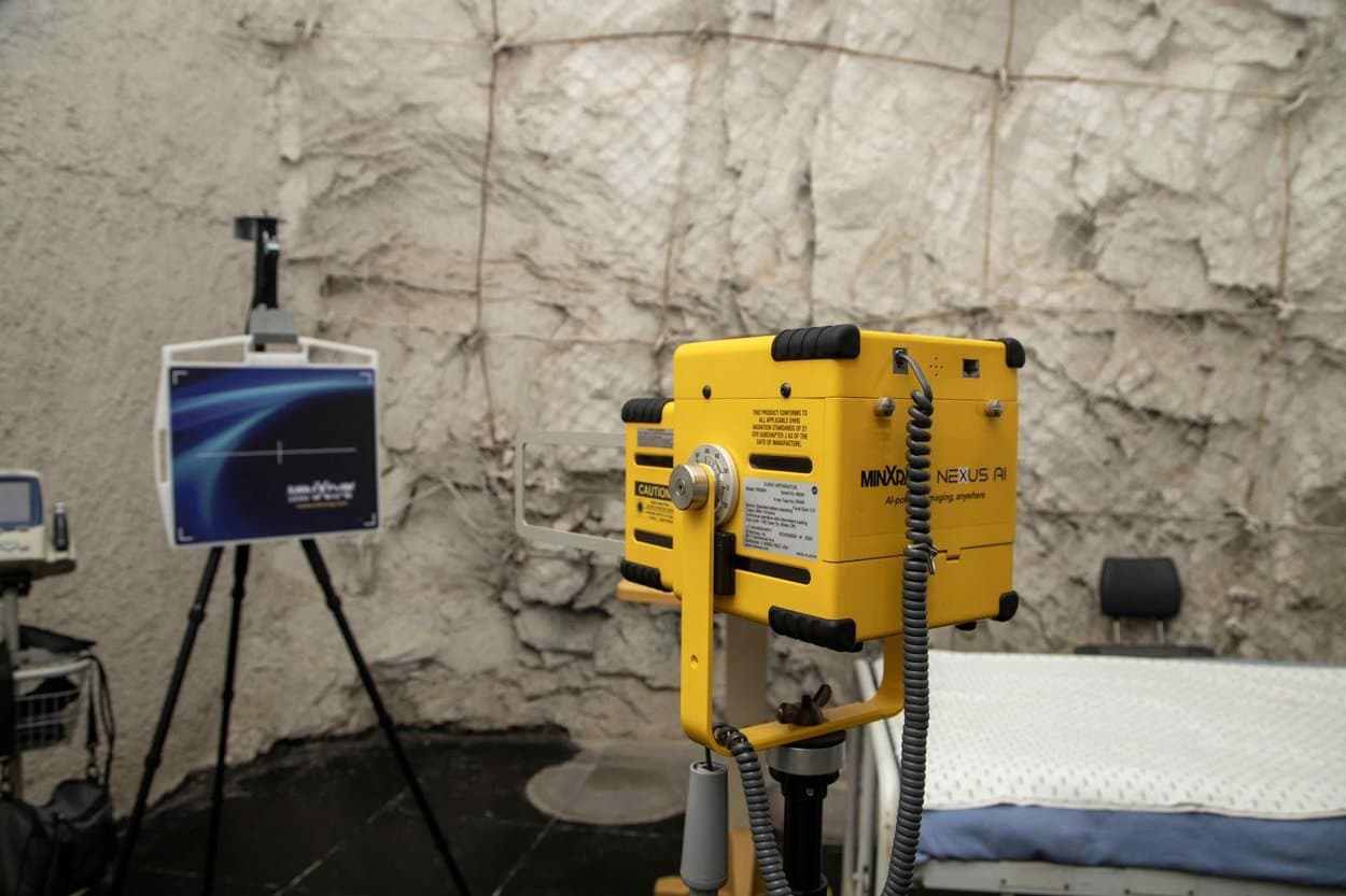 A yellow MinXray Nexus AI portable imaging device on a stand, positioned near a digital display screen.